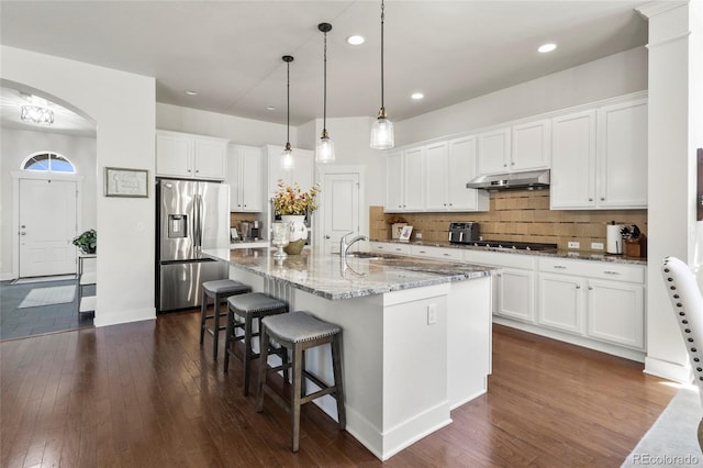 kitchen featuring under cabinet range hood, white cabinetry, stainless steel fridge with ice dispenser, dark wood-type flooring, and arched walkways