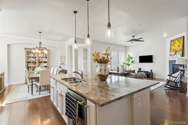 kitchen with dark wood-type flooring, a kitchen island with sink, a sink, and ceiling fan with notable chandelier