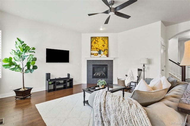 living area with stairs, wood finished floors, ceiling fan, arched walkways, and a tiled fireplace