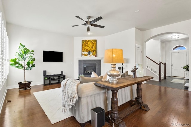 living room with visible vents, ceiling fan, arched walkways, dark wood-style floors, and stairs