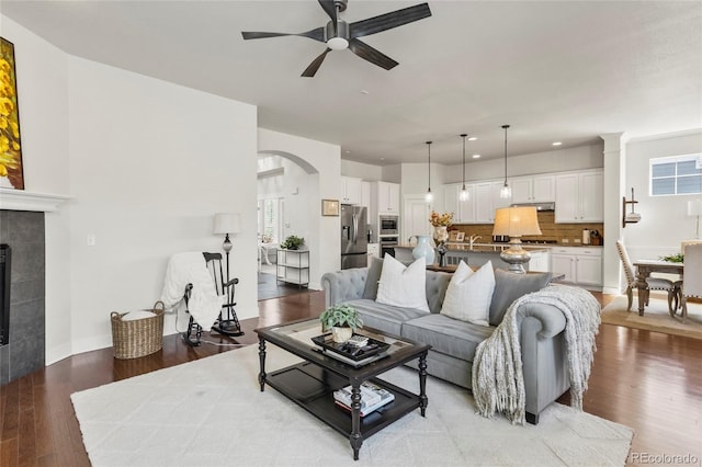 living area with a tile fireplace, arched walkways, ceiling fan, light wood-style floors, and recessed lighting