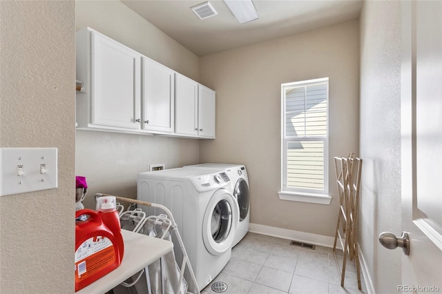 clothes washing area with washing machine and dryer, light tile patterned floors, cabinet space, visible vents, and baseboards