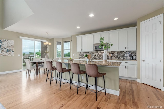 676 Fossil Bed Cir, Erie, CO 80516 - kitchen with stainless steel microwave, decorative backsplash, a center island with sink, light wood-style floors, and a kitchen breakfast bar