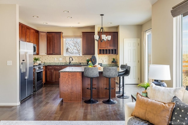 kitchen with a breakfast bar area, stainless steel appliances, a sink, open floor plan, and tasteful backsplash