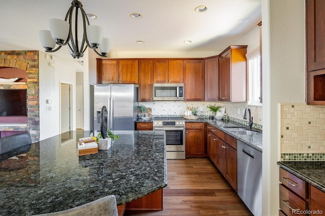 kitchen with decorative backsplash, appliances with stainless steel finishes, a sink, dark stone countertops, and wood finished floors