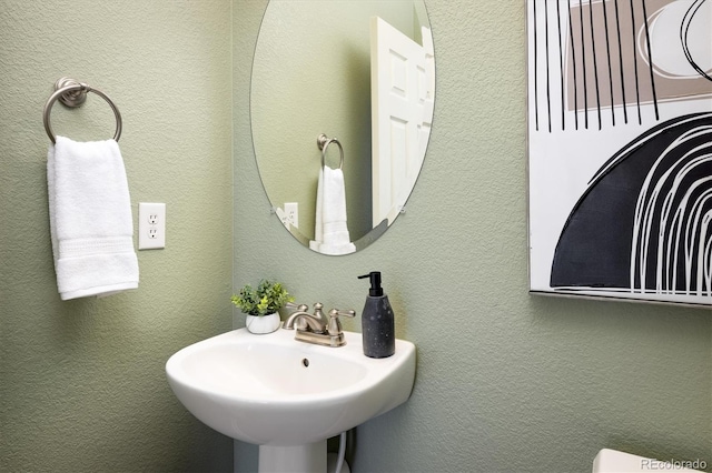 half bathroom with a textured wall and a sink