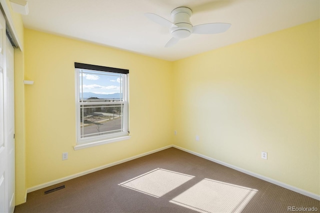 carpeted spare room featuring baseboards, visible vents, and ceiling fan