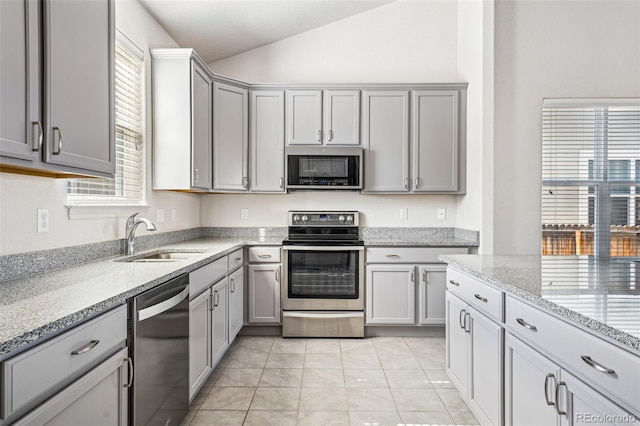 kitchen featuring light stone counters, lofted ceiling, gray cabinetry, appliances with stainless steel finishes, and a sink