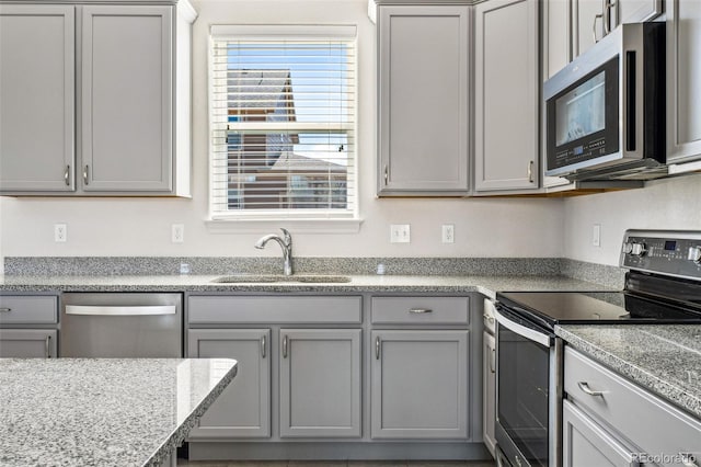 kitchen featuring stainless steel appliances, gray cabinets, a sink, and light stone countertops