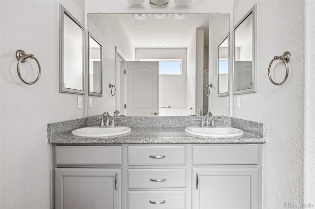 full bath featuring double vanity, a sink, and a textured wall