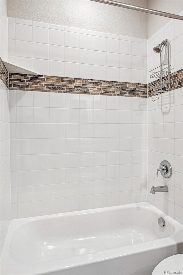 bathroom with washtub / shower combination and a textured wall