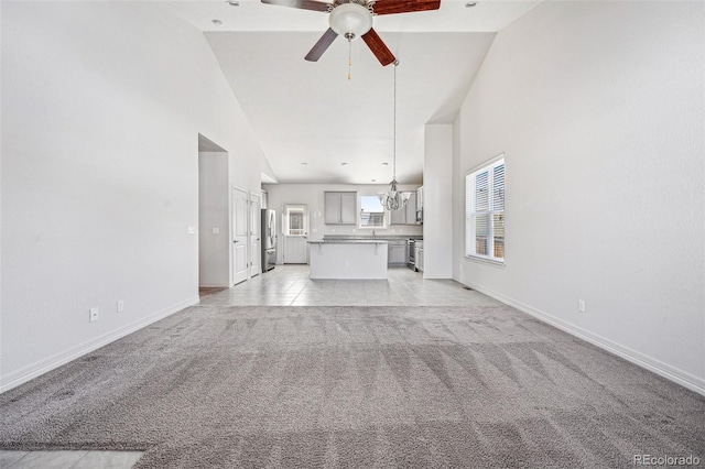 unfurnished living room featuring baseboards, ceiling fan with notable chandelier, high vaulted ceiling, and light colored carpet