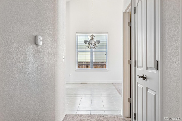 corridor with a chandelier, a textured wall, baseboards, and light tile patterned floors