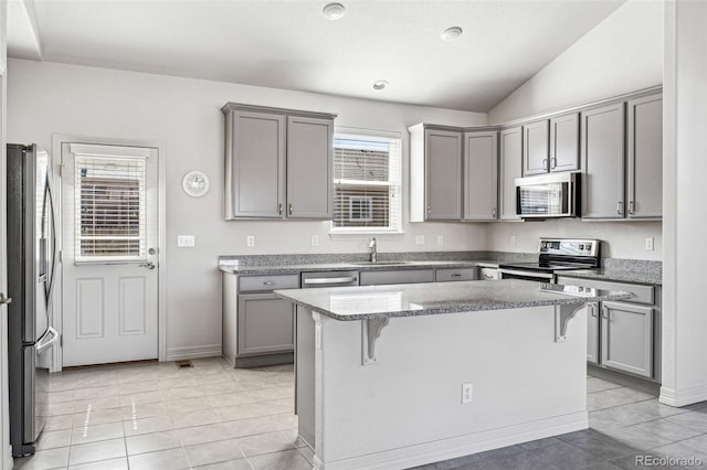 kitchen featuring appliances with stainless steel finishes, a kitchen bar, a sink, and gray cabinetry