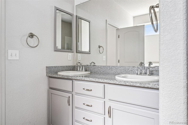 bathroom with a textured wall, double vanity, and a sink