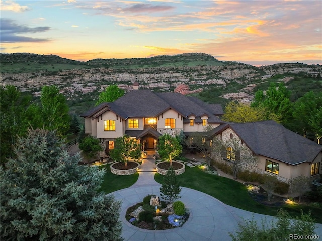9650 S Cougar Rd, Littleton, CO 80127 - view of front of property featuring stucco siding, curved driveway, stone siding, a chimney, and a front lawn