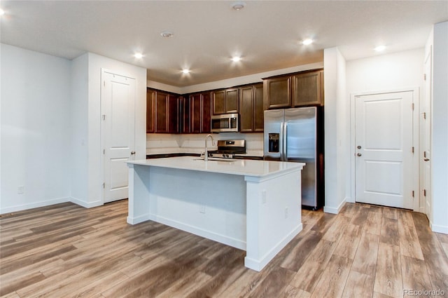 kitchen featuring a center island with sink, sink, dark brown cabinets, light hardwood / wood-style floors, and stainless steel appliances