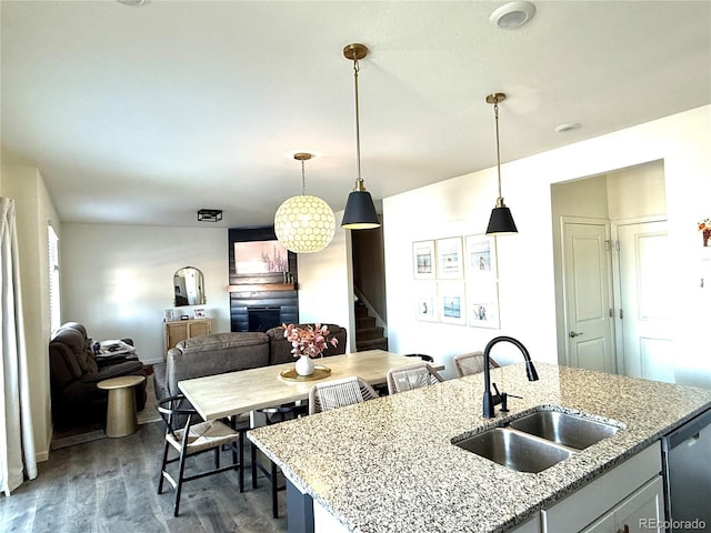 kitchen with pendant lighting, sink, dishwasher, light stone counters, and a fireplace