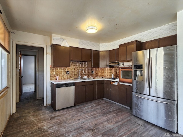 kitchen with a sink, extractor fan, light countertops, appliances with stainless steel finishes, and dark wood-style flooring