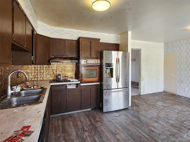 kitchen with a sink, appliances with stainless steel finishes, wallpapered walls, dark brown cabinets, and dark wood-style flooring