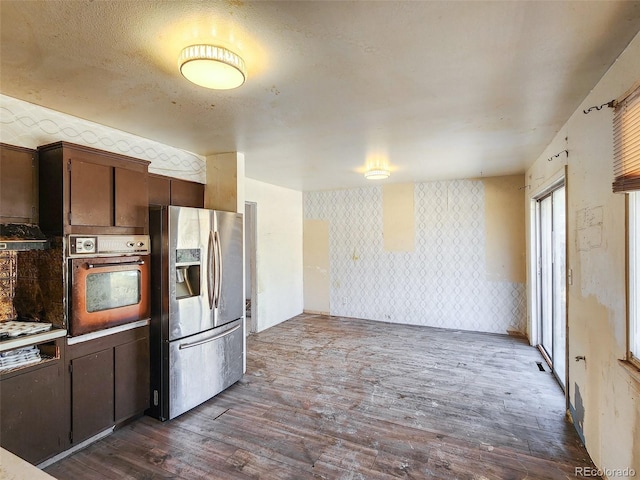 kitchen with wallpapered walls, dark wood-type flooring, dark brown cabinets, stainless steel refrigerator with ice dispenser, and wall oven