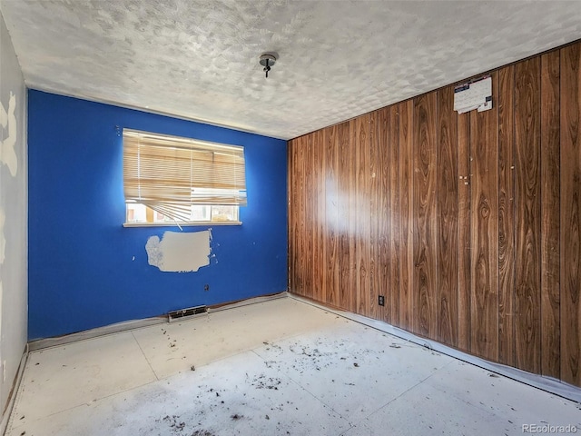 spare room featuring wooden walls, a textured ceiling, and visible vents