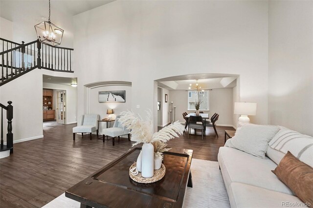 living room with stairs, arched walkways, an inviting chandelier, and wood finished floors