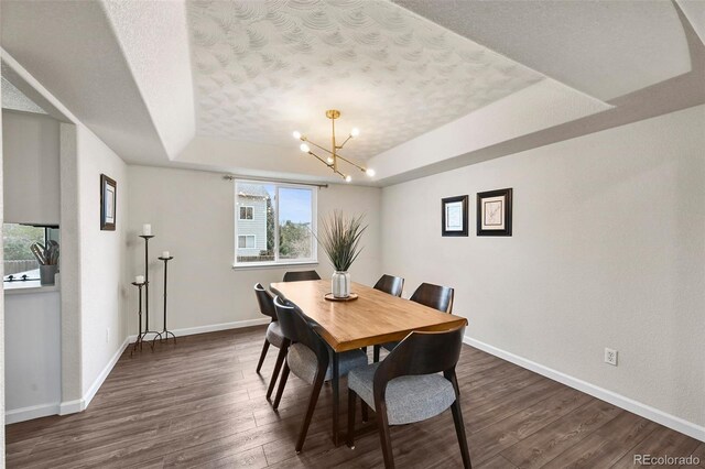 dining space with dark wood finished floors, a raised ceiling, baseboards, and a notable chandelier