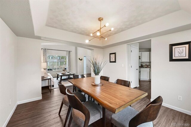 dining room featuring baseboards, dark wood-type flooring, a raised ceiling, and a chandelier