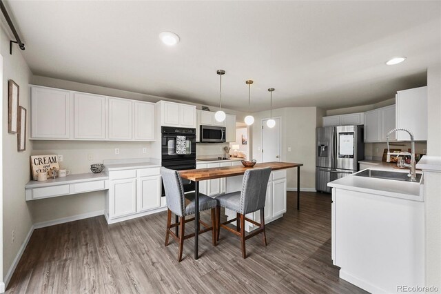 kitchen featuring built in desk, wood finished floors, a sink, black appliances, and butcher block counters