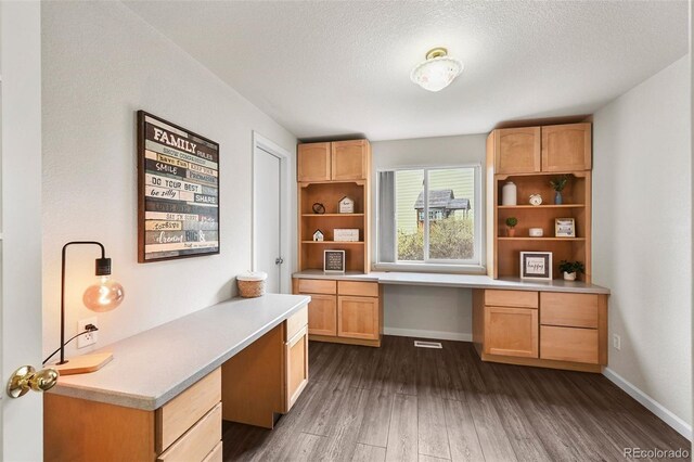 home office with a textured ceiling, baseboards, built in study area, and dark wood-type flooring