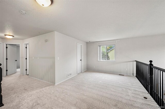 unfurnished room featuring carpet flooring, a textured ceiling, visible vents, and baseboards