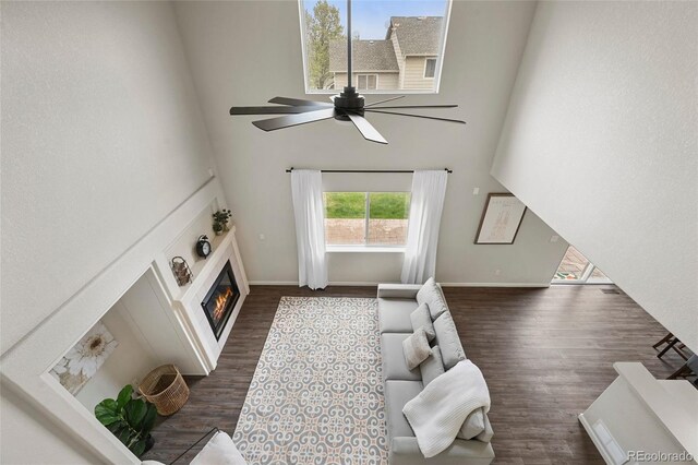 living area featuring a glass covered fireplace, a high ceiling, a ceiling fan, and dark wood-style floors