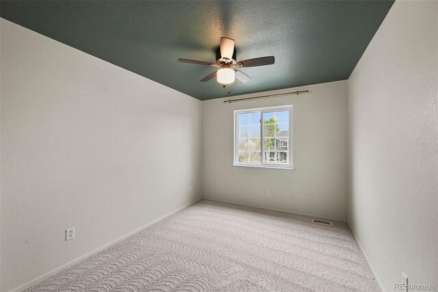 carpeted spare room with baseboards, ceiling fan, and visible vents