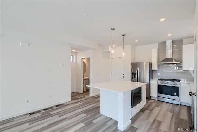 kitchen with appliances with stainless steel finishes, wall chimney range hood, decorative light fixtures, white cabinets, and a center island