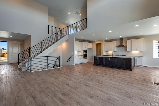 kitchen featuring wall chimney range hood, sink, an island with sink, and light hardwood / wood-style floors