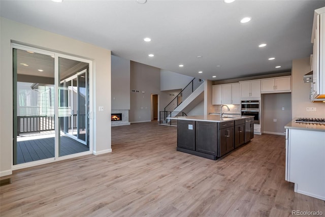 kitchen with light wood-type flooring, dark brown cabinets, appliances with stainless steel finishes, and an island with sink