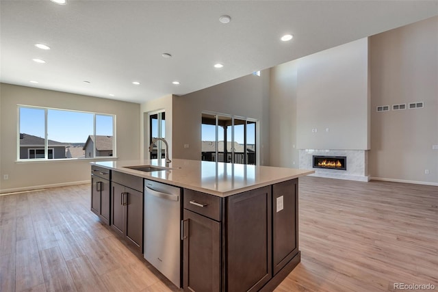 kitchen featuring a premium fireplace, sink, an island with sink, stainless steel dishwasher, and light wood-type flooring