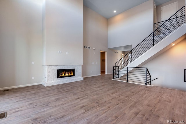 unfurnished living room featuring a premium fireplace, light hardwood / wood-style flooring, and a high ceiling