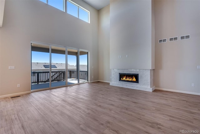 unfurnished living room with a high ceiling, light wood-type flooring, a wealth of natural light, and a premium fireplace