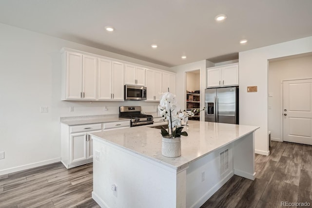 kitchen featuring stainless steel appliances, dark hardwood / wood-style floors, light stone countertops, white cabinets, and a center island with sink