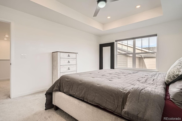 bedroom with ceiling fan, light colored carpet, and a tray ceiling