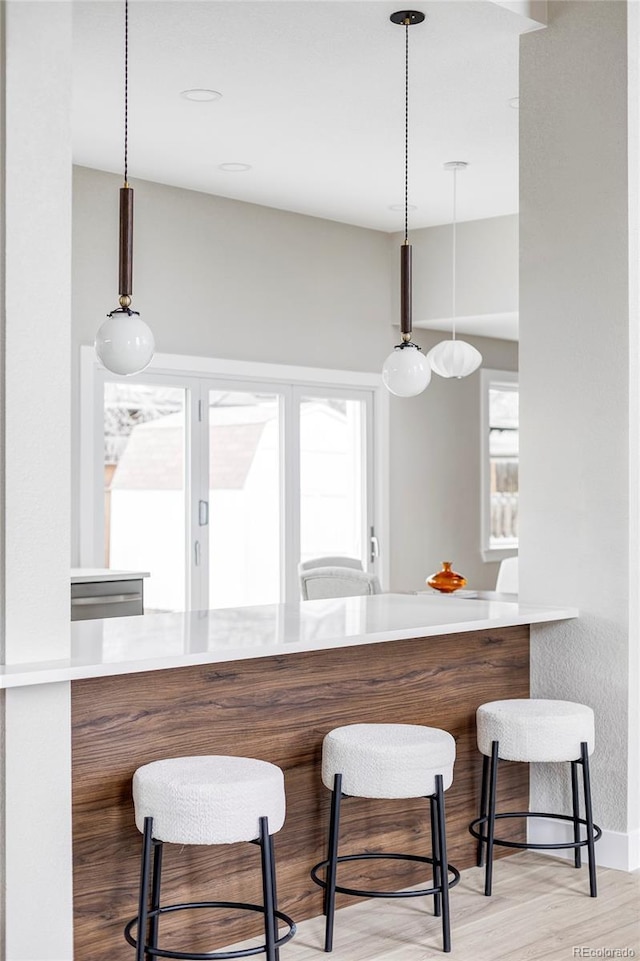 kitchen with a breakfast bar, kitchen peninsula, hanging light fixtures, and light hardwood / wood-style flooring