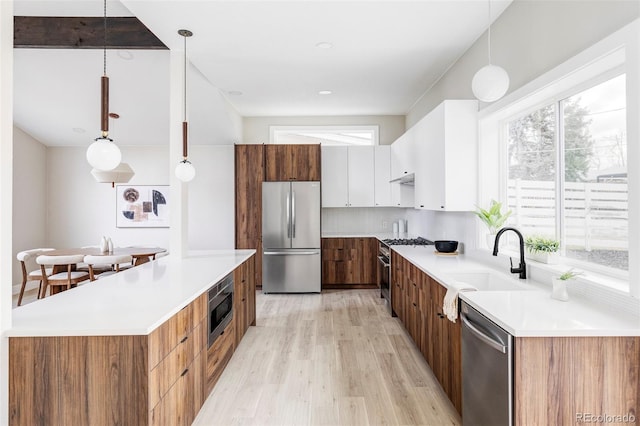 kitchen featuring appliances with stainless steel finishes, hanging light fixtures, sink, white cabinets, and plenty of natural light