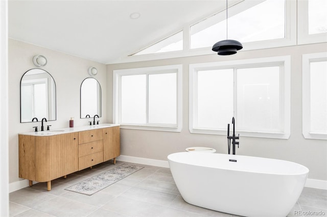 bathroom with tile patterned floors, a tub, vanity, and vaulted ceiling