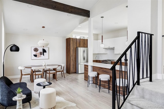 interior space featuring pendant lighting, vaulted ceiling with beams, white cabinetry, and stainless steel refrigerator