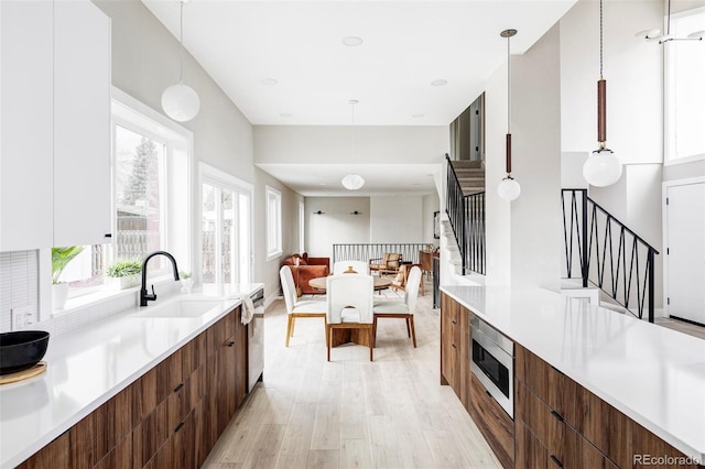 kitchen featuring sink, hanging light fixtures, stainless steel appliances, light hardwood / wood-style flooring, and white cabinets