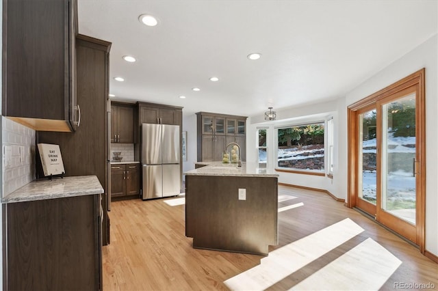 kitchen featuring backsplash, stainless steel refrigerator, a center island with sink, and light wood-type flooring