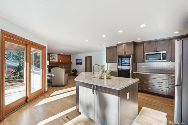 kitchen featuring dark brown cabinetry, light stone countertops, light hardwood / wood-style flooring, a kitchen island with sink, and appliances with stainless steel finishes