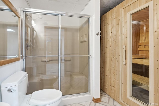 bathroom featuring toilet, a shower with shower door, and wooden walls